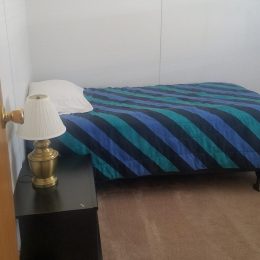 A small bedroom with a single bed featuring blue and black striped bedding, a bedside table, and a lamp next to the bed.